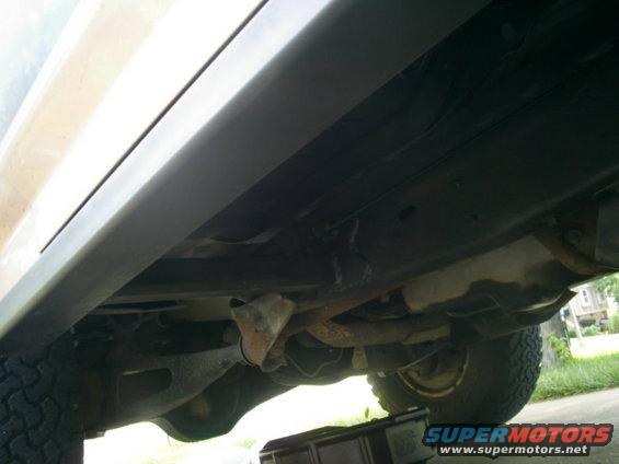 Underside of a vehicle showing the frame, exhaust, and tire