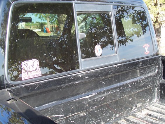 Black pickup truck bed with a sliding rear window showing reflections of trees and a playground; Alabama and Texas stickers on the window