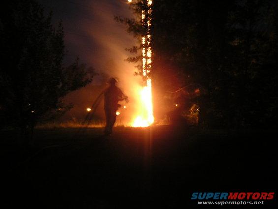 person with hose near large fire at night