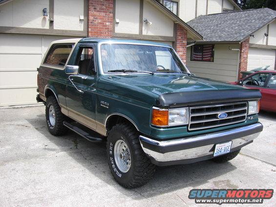 Green Ford Bronco with tan lower body trim and a tan removable roof, parked in a driveway