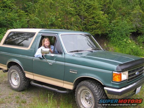 Green 1990 Ford Bronco with tan trim and a woman driving