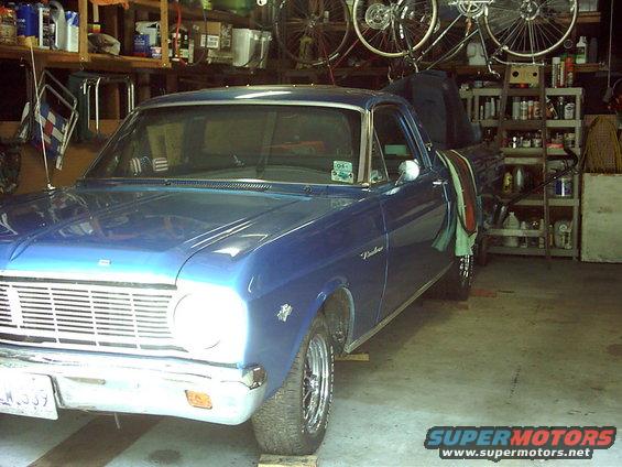 Blue 1966 Ford Ranchero pickup truck with chrome grille, parked indoors on wooden blocks