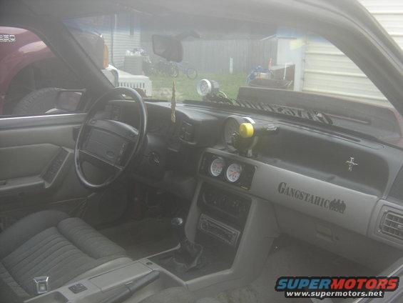 Interior of a 1988 Ford Mustang with aftermarket gauges and 'Gangstahic' decal on the dash