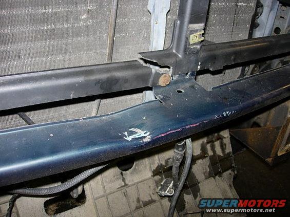 Dark blue bumper support with white scuff marks and pink paint transfer, showing damage and wiring. Radiator visible behind