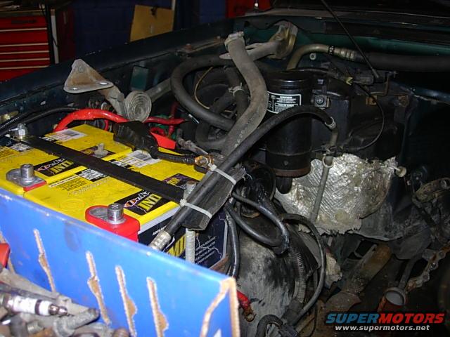Engine bay with dual yellow Optima batteries, hoses, and wiring. Green vehicle exterior visible