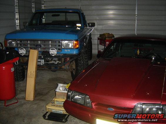 Blue pickup truck with HELLA lights and a red coupe parked in a garage