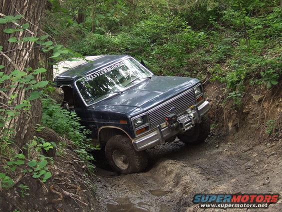 Dark blue SUV with a winch on a muddy trail, tires deep in the mud, leaning to the side