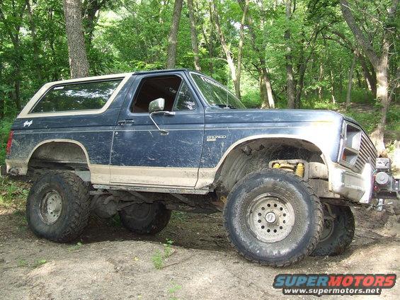 Blue and tan Ford Bronco with large off-road tires, lifted suspension, and visible dirt