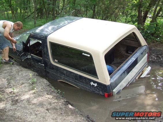 Dark blue and tan Ford Bronco stuck in mud with a man by the driver's door