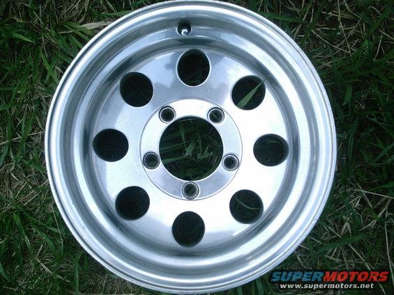 Aluminum wheel with ten circular cutouts and a five-lug bolt pattern, lying on grass