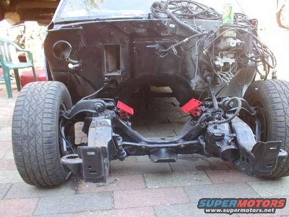 Car's front end stripped down, showing frame, suspension, and engine bay