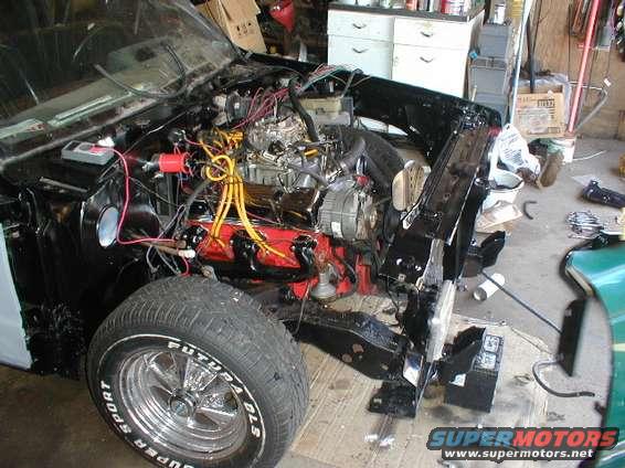 Car engine bay with exposed engine, wiring, and front tire. Chrome wheel with "SUPER SPORT" text