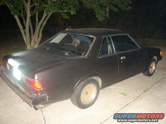 Black coupe, rear 3/4 view, gold mesh wheels