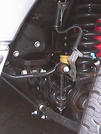 Close-up of a truck's front suspension with black springs, yellow bump stops, and metal linkages
