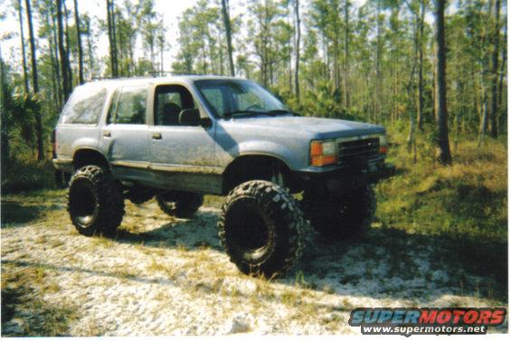 Silver lifted Ford Explorer with large off-road tires parked on a sandy trail