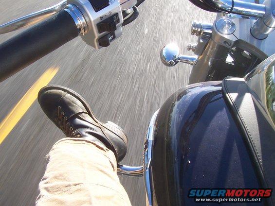 Rider's boot and tan pants on a motorcycle, view of handlebars and dashboard
