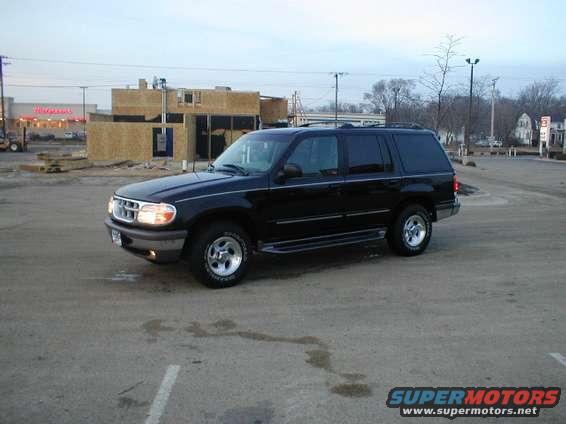 Black SUV parked on asphalt, front 3/4 view. Construction site in background