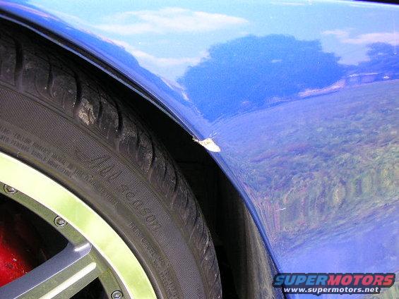 Close-up of a blue car's fender above a tire. There's a small chip on the fender