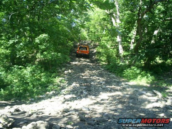 Orange SUV driving up a rocky, wooded trail