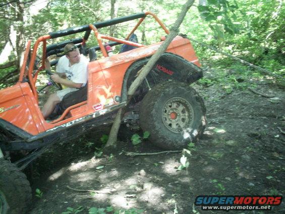 Orange off-road vehicle with roll cage stuck on a dirt trail, driver visible