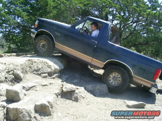 Dark blue Ford Bronco with tan trim navigating rocky terrain