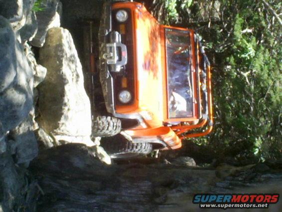 orange off-road vehicle tipped onto its side in rocks and trees