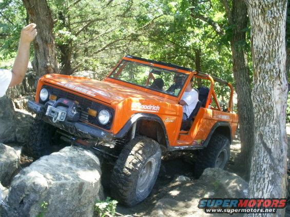 Orange SUV with BFGoodrich tires navigating large rocks on a trail. Driver is visible inside