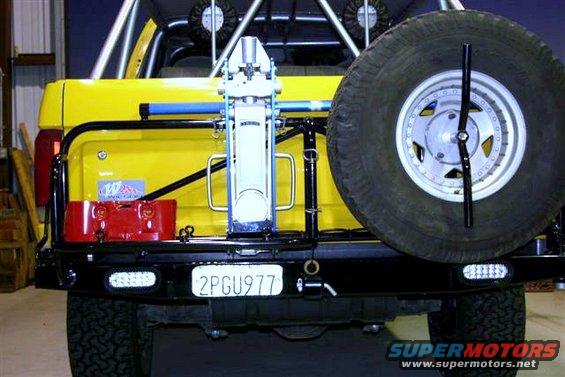 Yellow SUV rear bumper with spare tire, jack, red gas can, and license plate 2PGU977