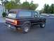 1991 Ford Bronco - A black Ford Bronco is shown from the rear three-quarter view on a paved road in front of houses and trees.