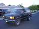 1991 Ford Bronco - A black Ford Bronco drives down a suburban street, with another Ford truck in the background.