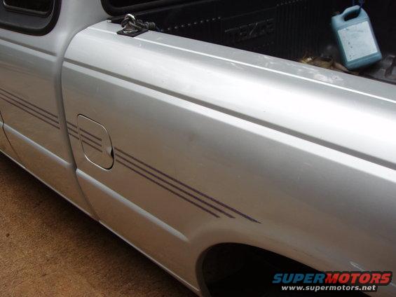 Silver 1994 Mazda B3000 pickup truck side view showing fuel door and stripe detail. Bed has a blue jug