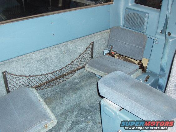 Interior rear of a pickup truck showing jump seats, carpeted floor, and storage net
