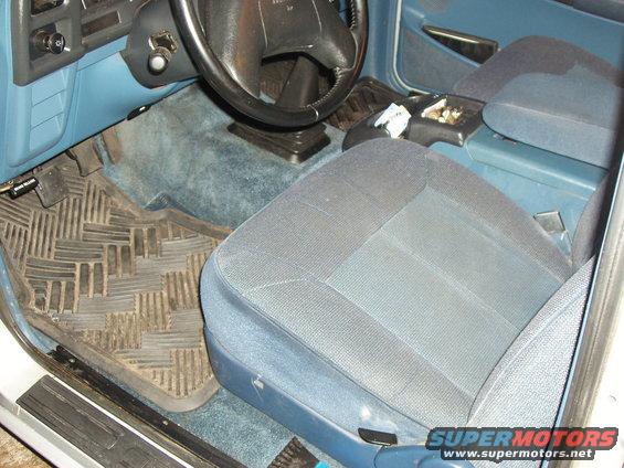 Truck interior with blue cloth seats, black steering wheel, and rubber floor mats. The dashboard is visible