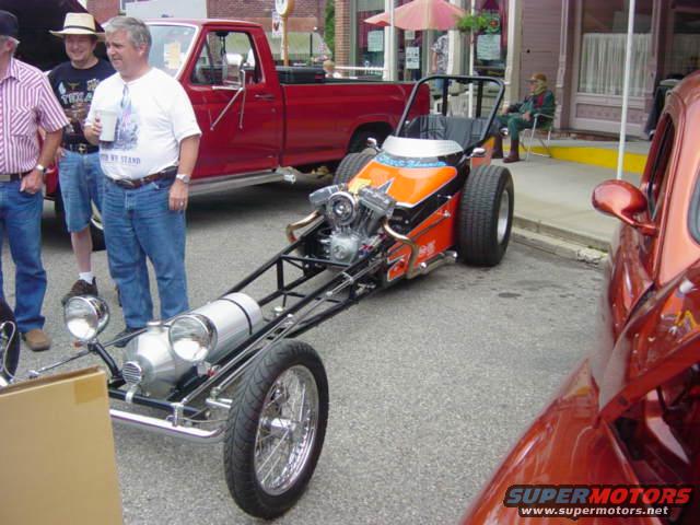 Dragster with orange bodywork and exposed engine, parked on asphalt