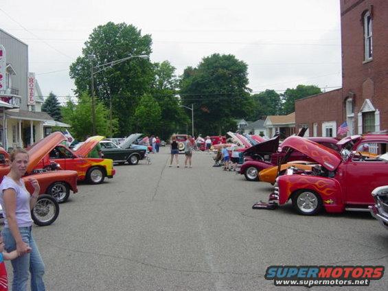Street scene with many cars with hoods up at a car show, a woman and child in foreground
