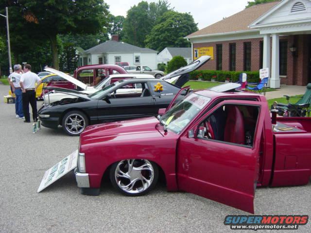 red pickup truck with doors open, lowered, next to black sports car with hood up at car show