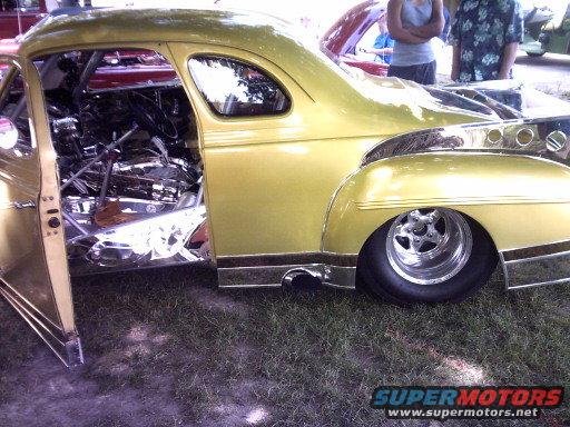 Yellow classic coupe with open door showing custom interior and chrome engine parts. Wide rear tire and chrome wheels