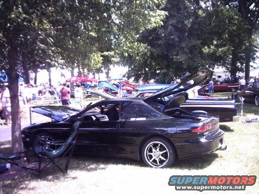 Black coupe with hoods open, parked on grass at an outdoor event. Chrome wheels visible