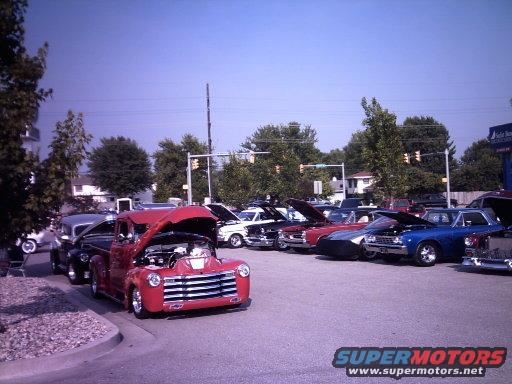 Red classic pickup truck with hood open, parked next to other cars at an outdoor car show