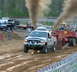 2000 Ford F-250 - A silver 2000 Ford F-250 truck emits dark smoke while competing in a pull event with a red sled.