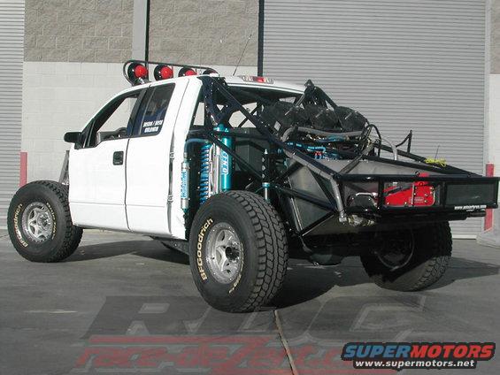 White custom off-road truck with roll cage and large tires. Some text visible on door