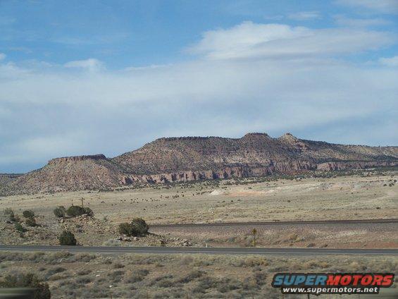Desert landscape with mesas and a road under a cloudy sky