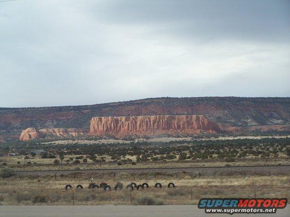 Desert landscape with layered rock formations under a cloudy sky. Railroad tracks and scattered tires are in the foreground