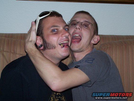 Two guys making faces on a couch, one with piercings and sunglasses on his head, the other with glasses