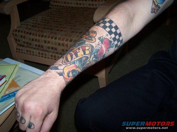 Tattooed forearm with checkered band, banner reading 'OFB', and other colorful designs