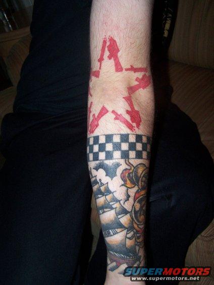 Tattoo of a red star with guns, checkerboard band, and sailing ship on an arm