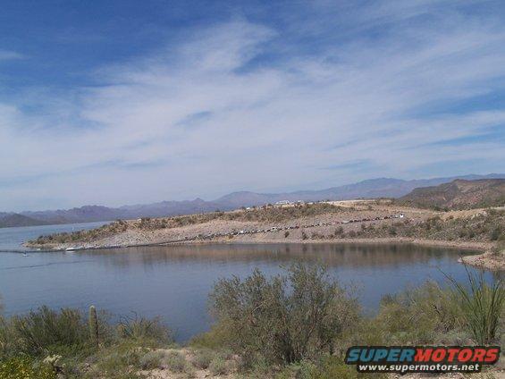 Cars parked along a desert lake shore with mountains in the background