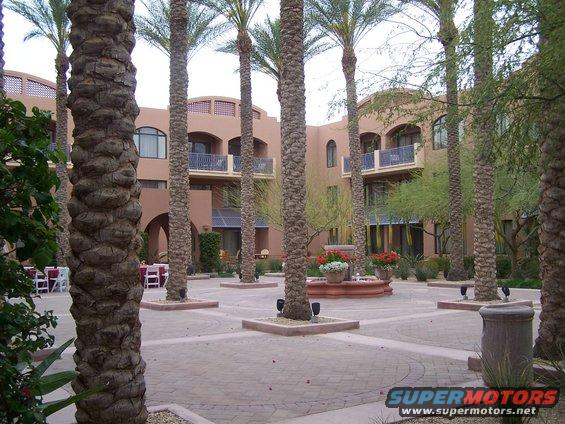 Courtyard with palm trees, fountain, and a tan building with balconies