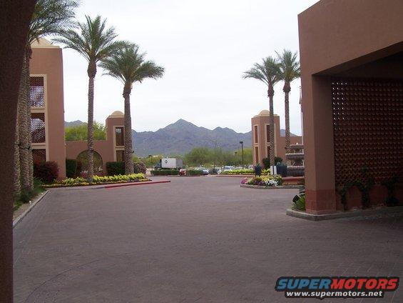 Resort entrance with palm trees, fountains, and mountains in the background