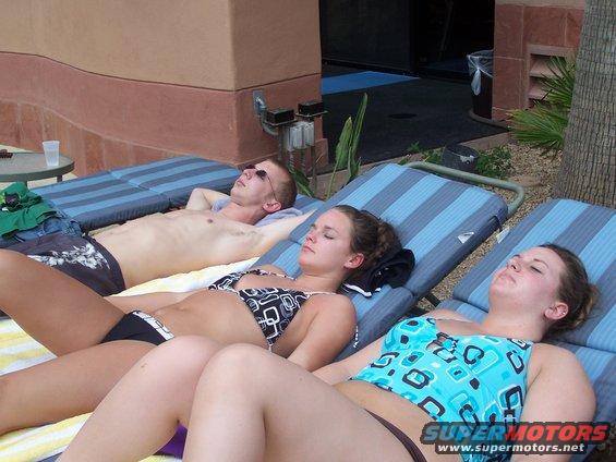 Three people sunbathing on lounge chairs by a pool